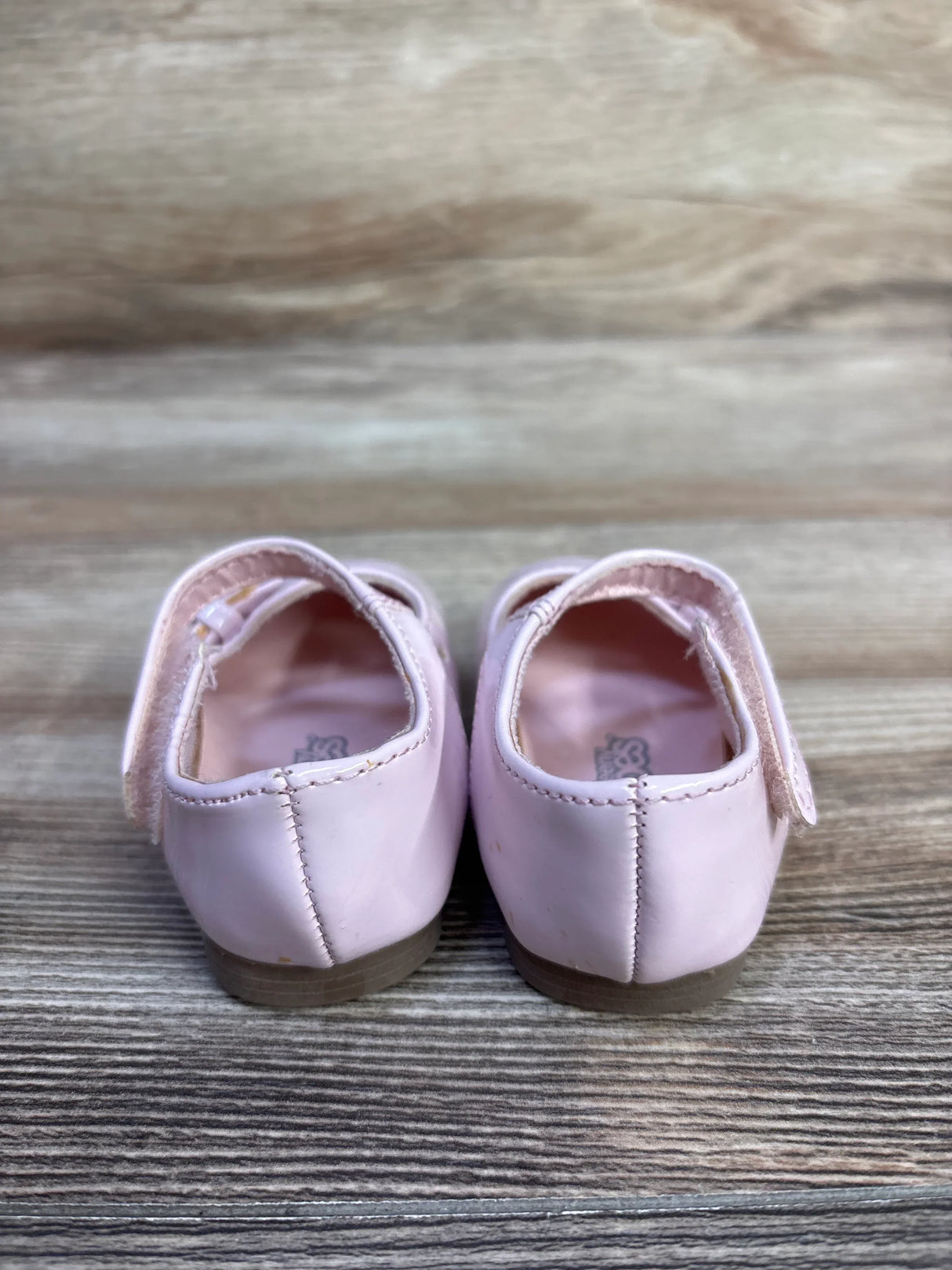 Rear view of Teeny Toes pink patent Mary Jane flats showing Velcro straps and low heels on wood surface