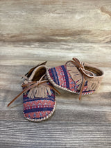 Patterned baby moccasins with suede fringe and laces on wooden background