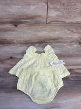 Top-down view of yellow two-piece baby set with ruffled sleeveless top and elastic bloomers on wood background