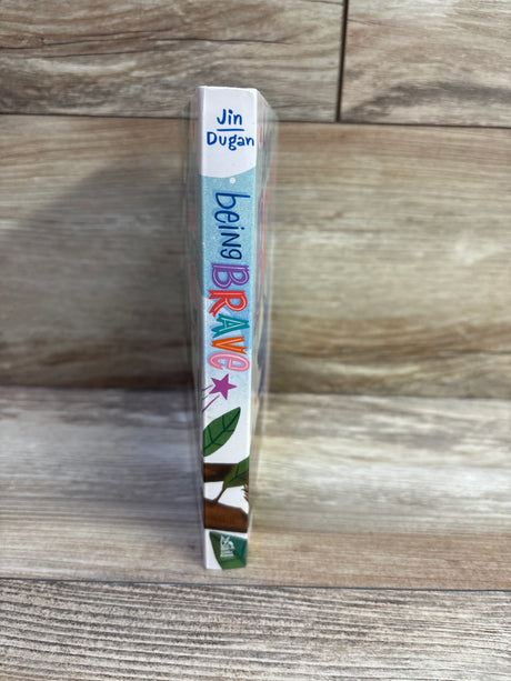 Side view of Being Brave board book showing colorful vertical title on the spine and leaf illustration against wood background