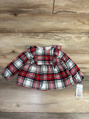 Red plaid baby girl top with ruffled sleeves and tag, laid on wood floor