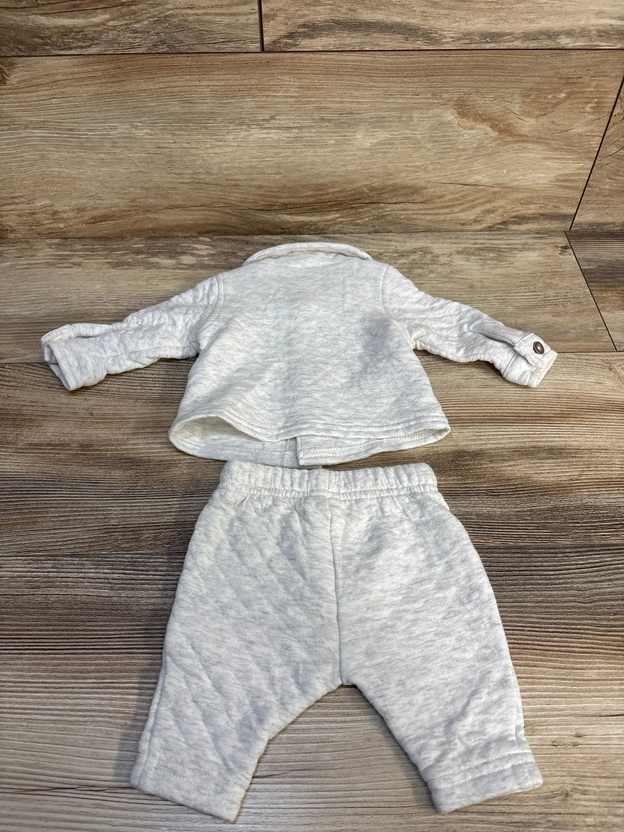 Light gray baby outfit with quilted long sleeve top and pants on wood background