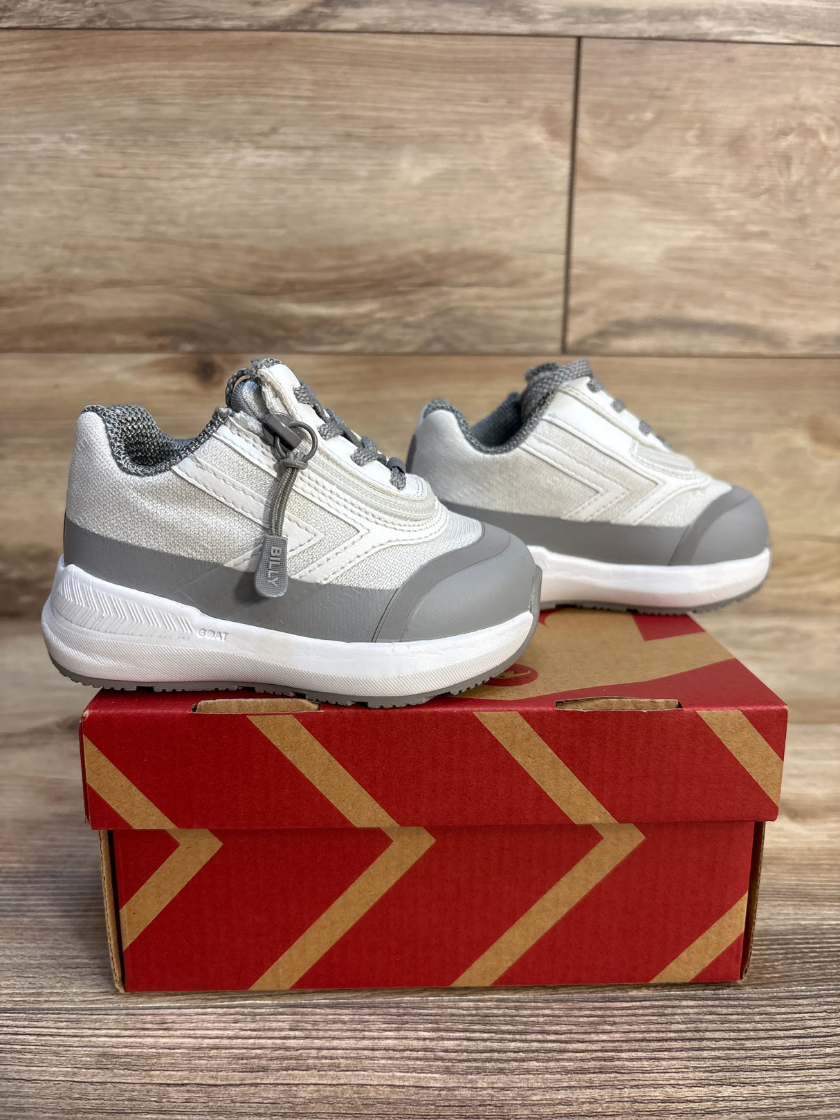 Gray and white toddler sneakers with rubber soles on a red shoebox, wooden background