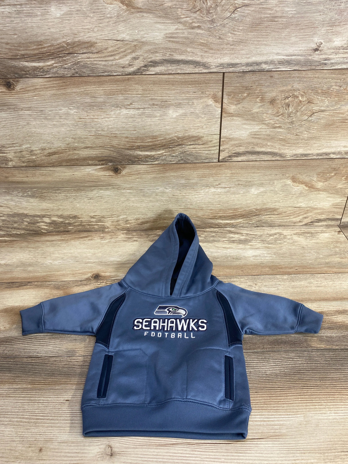 Toddler-sized blue Seahawks football hoodie with front pockets on wooden floor