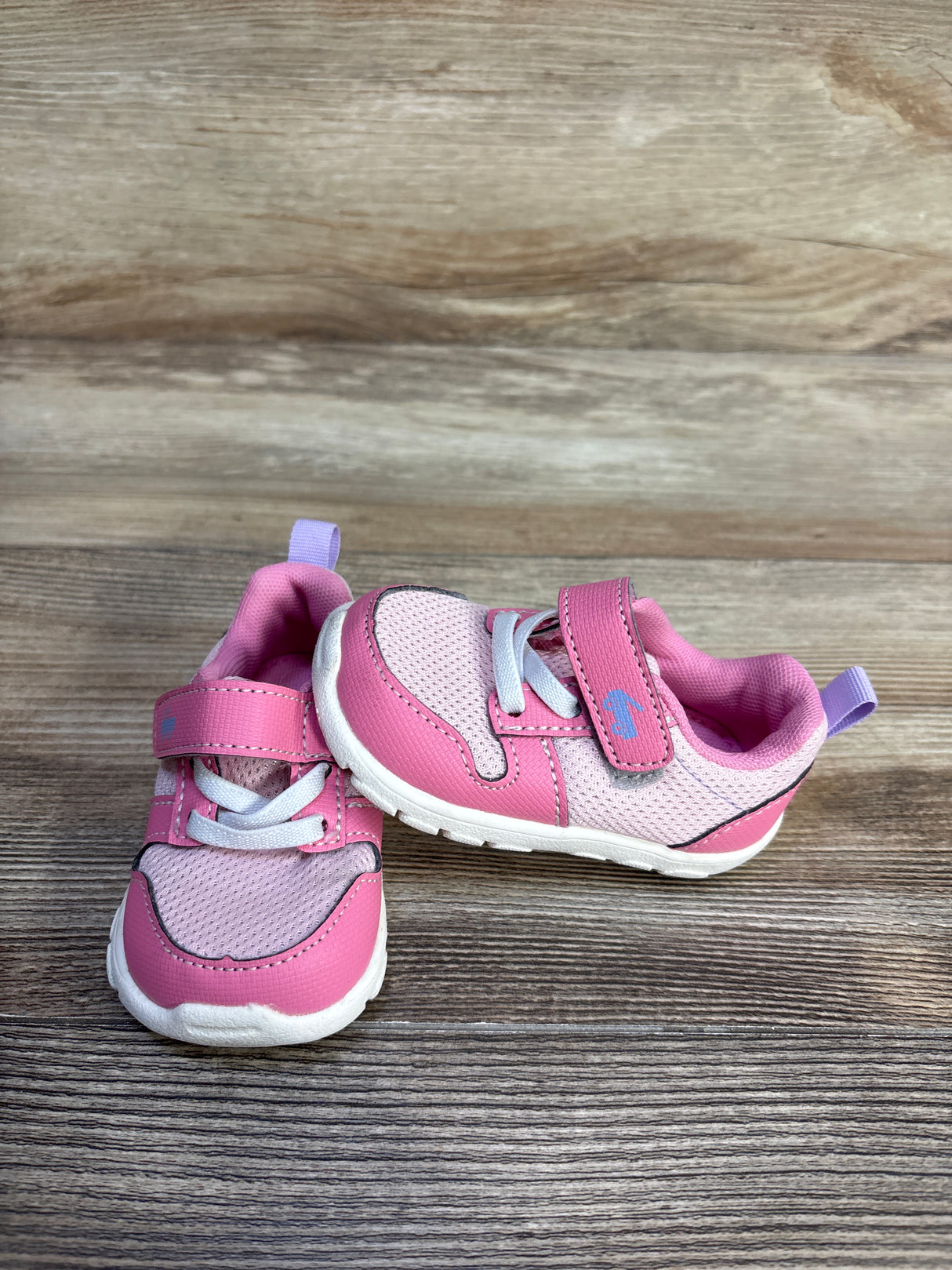 Three-quarter view of pink See Kai Run Tenny toddler sneakers showing mesh upper, velcro strap, elastic laces on wood
