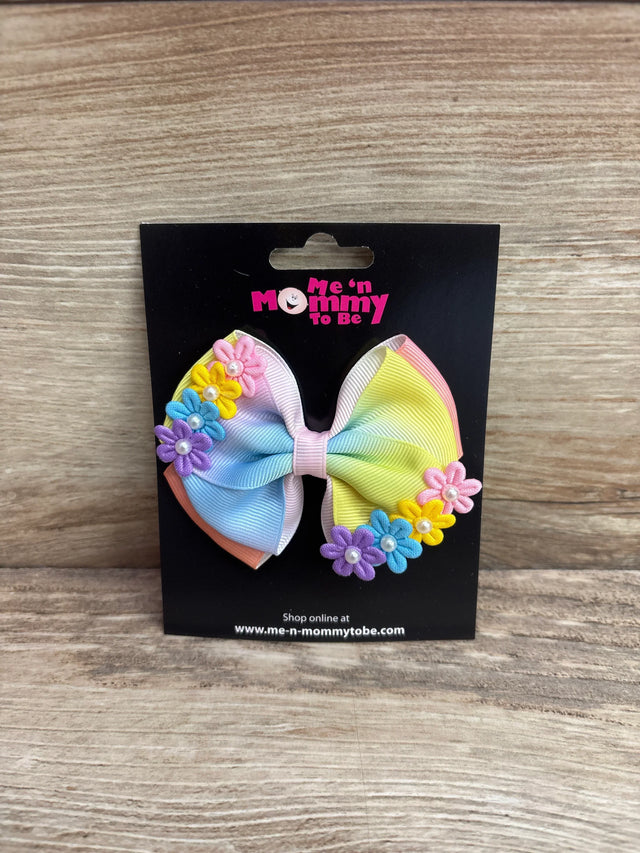 Front view of double layer yellow rainbow hair bow showing grosgrain ribbon layers and small fabric flower appliques with faux pearls on a black display card