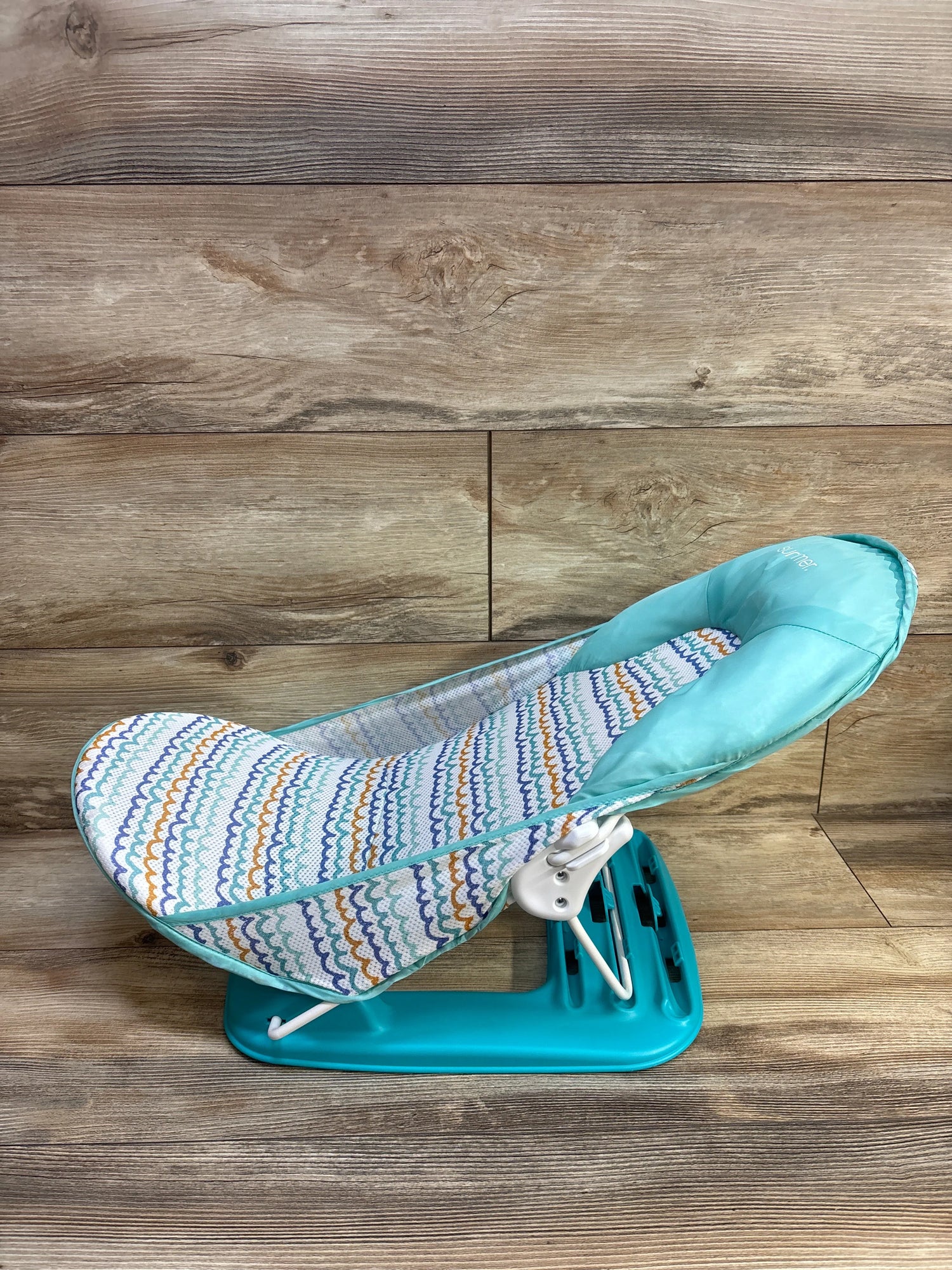 Side view of Summer Deluxe Baby Bather showcasing turquoise frame and patterned fabric seat on a wood plank background