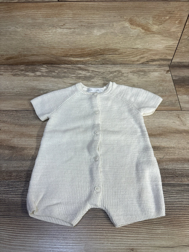 Top-down view of ivory knit shortie romper showcasing front button closure and ribbed knit texture on wood background