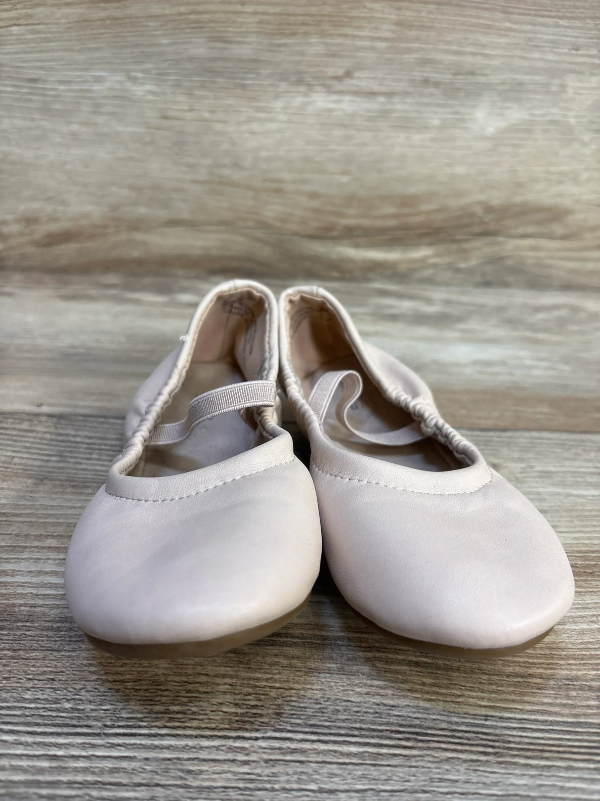 Light pink toddler ballet shoes with elastic straps on wood floor