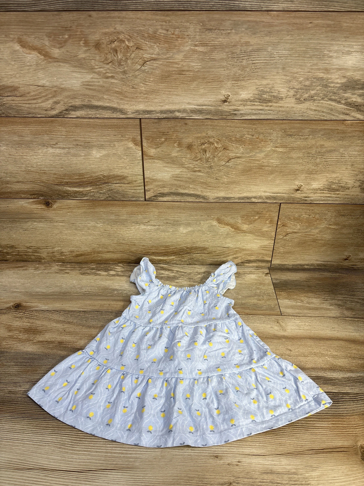 Flat lay of Just One You blue tiered toddler dress showcasing yellow floral print and ruffled shoulder straps on wood background