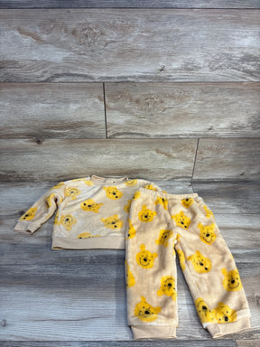 Plush beige toddler pajama set with yellow bear face print, laid on wood background