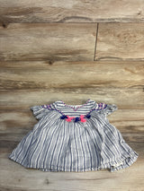 Striped baby dress with pink and navy tassel accents on wood background, gently used