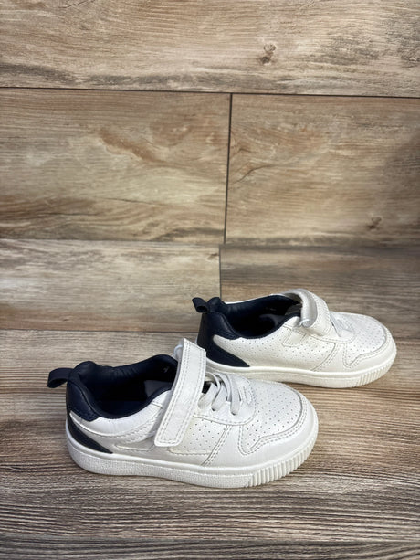 Side view of Carter's Every Step Port sneakers showing white perforated upper, navy heel, and Velcro strap on wood backdrop