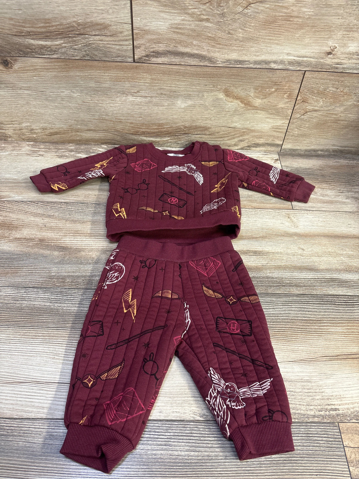Top down view of maroon Harry Potter two piece sweatshirt and pants set with an all over wizard themed print on wood flooring