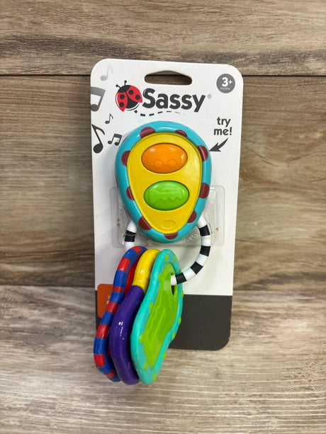 Front view of Sassy electronic keys showcasing colorful buttons and attached textured keys in retail packaging on a wood background