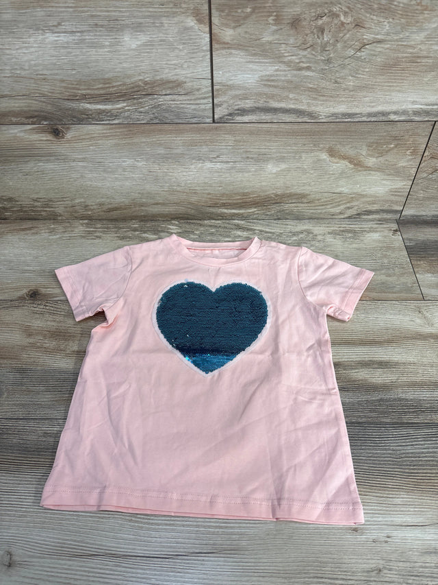 Light pink children’s short-sleeve t-shirt with large blue sequin heart on front, on wood floor