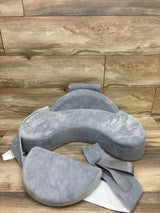 Front view of Momcozy CozyPro nursing pillow in grey showcasing contoured U shape and adjustable strap with wood background