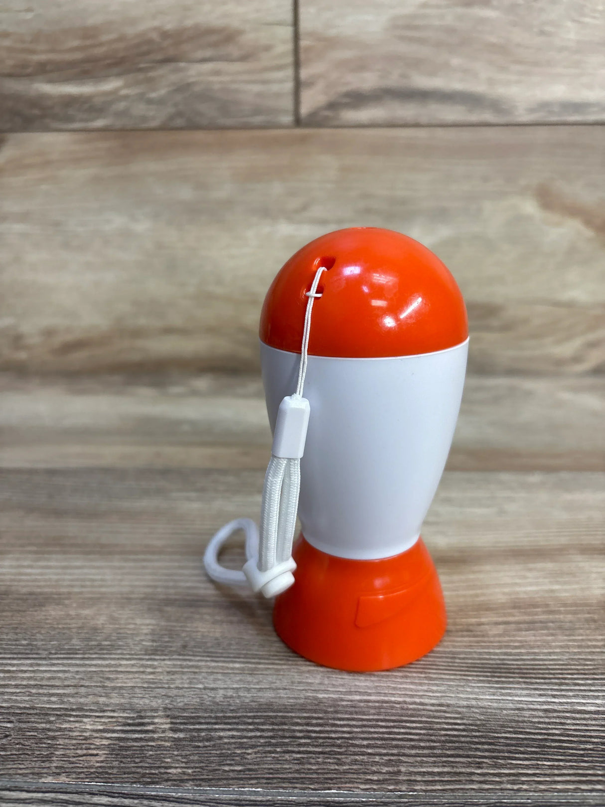 Front view of Baby Shusher sleep soother showing orange-and-white casing and wrist strap on wood tabletop