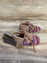 Patterned suede baby moccasins with fringe and laces on wooden background
