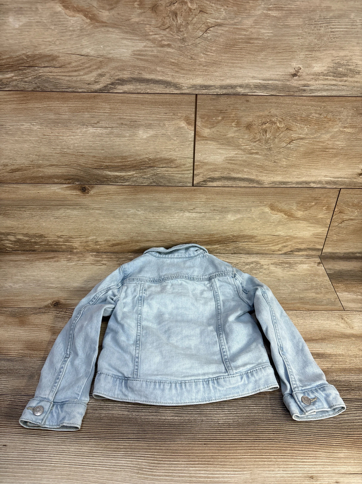 Back view of Cat & Jack light-wash denim toddler jacket, size 4T, showing back seam and button cuffs laid flat on wood floor