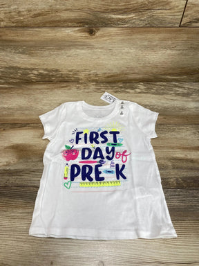 Flat lay of white Children's Place 3T short-sleeve shirt with FIRST DAY of PRE-K text and colorful school graphics on wood