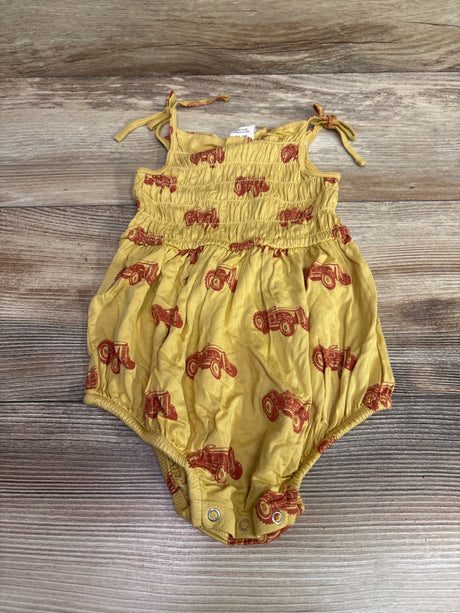 Front view of yellow Kate Quinn bamboo bubble romper with smocked bodice and red tractor print on wood