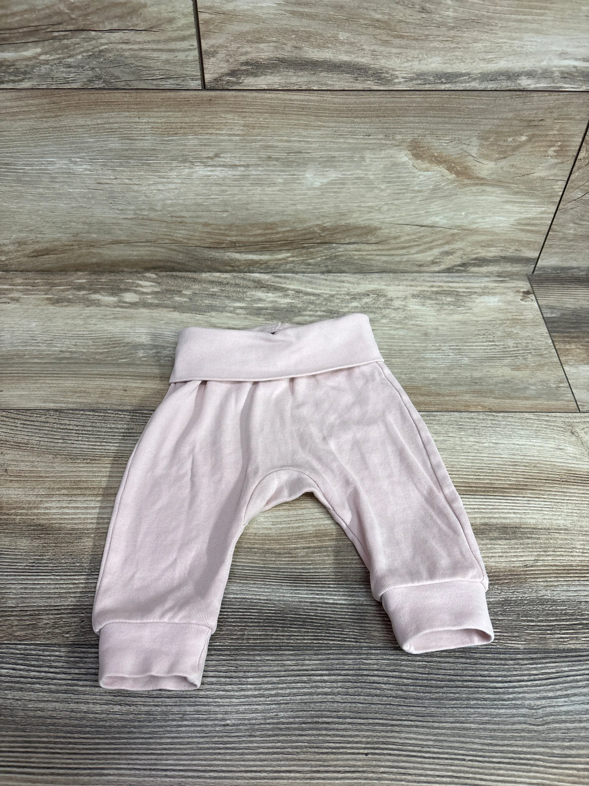 Flat lay of pink H&M foldover-waist baby pants showing fold-over waistband and cuffed legs on wood background