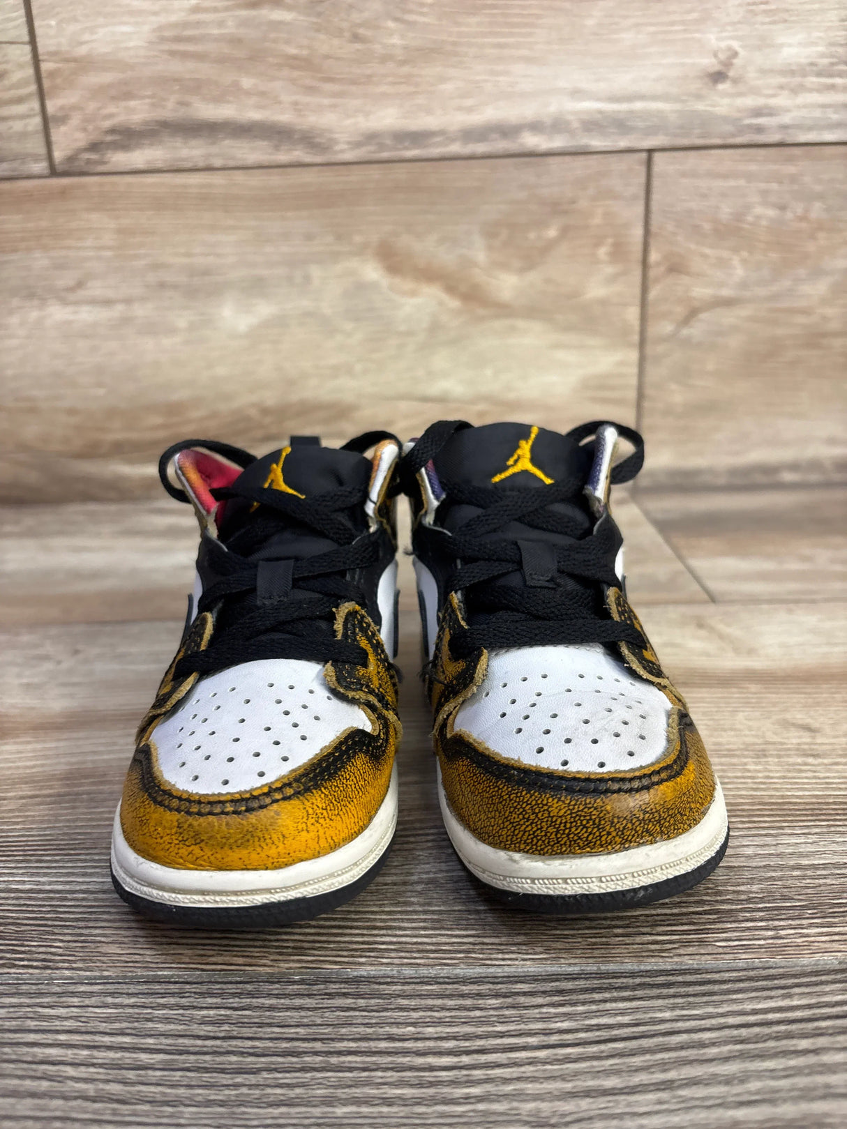 Front view of toddler Air Jordan 1 Mid SE Wear-Away Taxi sneakers, size 8C showcasing worn yellow overlays and black tongues on wood floor
