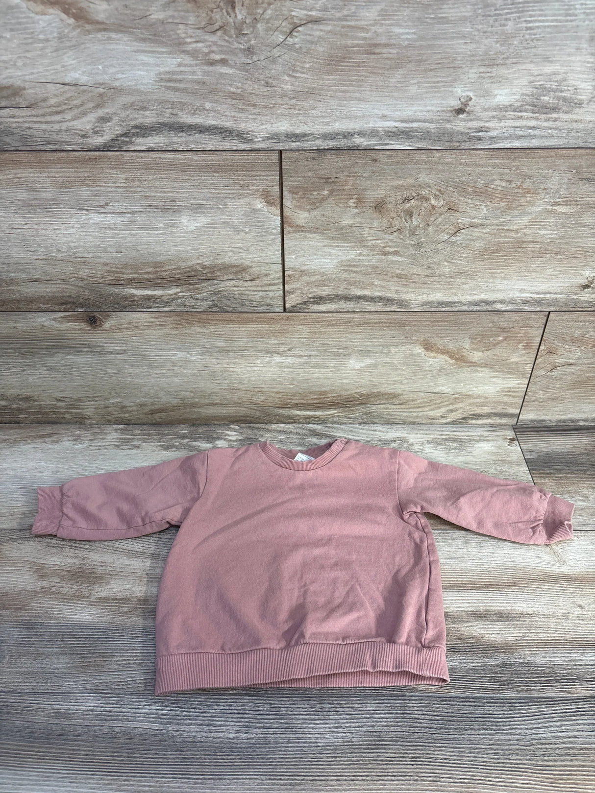 Flat-lay of H&M toddler pink pullover sweatshirt showcasing crewneck, ribbed cuffs and hem on light wood background