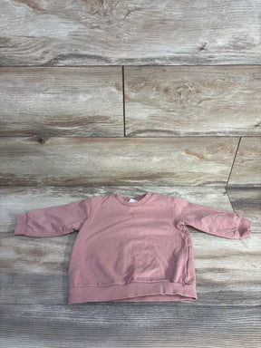 Flat-lay of H&M toddler pink pullover sweatshirt showcasing crewneck, ribbed cuffs and hem on light wood background