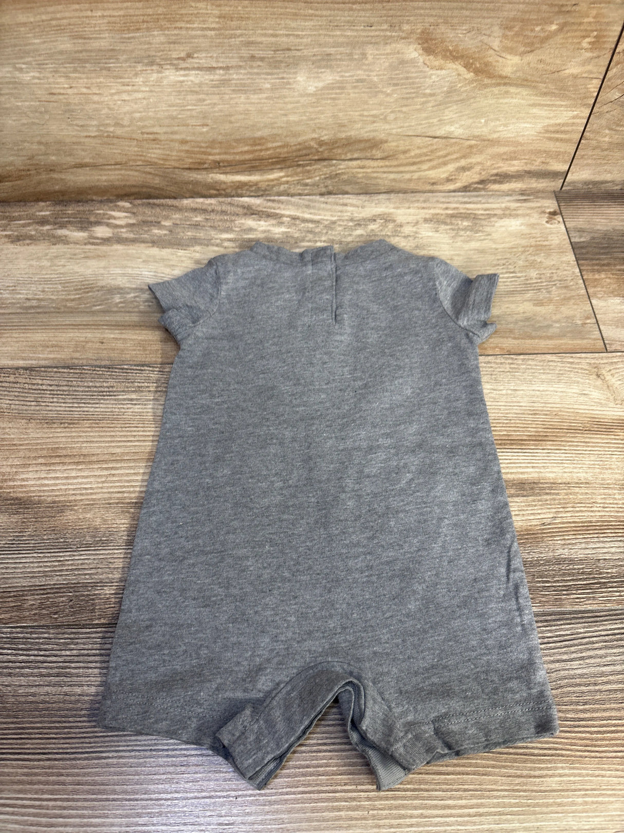 Flat lay of grey Nike shortie romper size 3M showing short sleeves and back snap placket on wood background