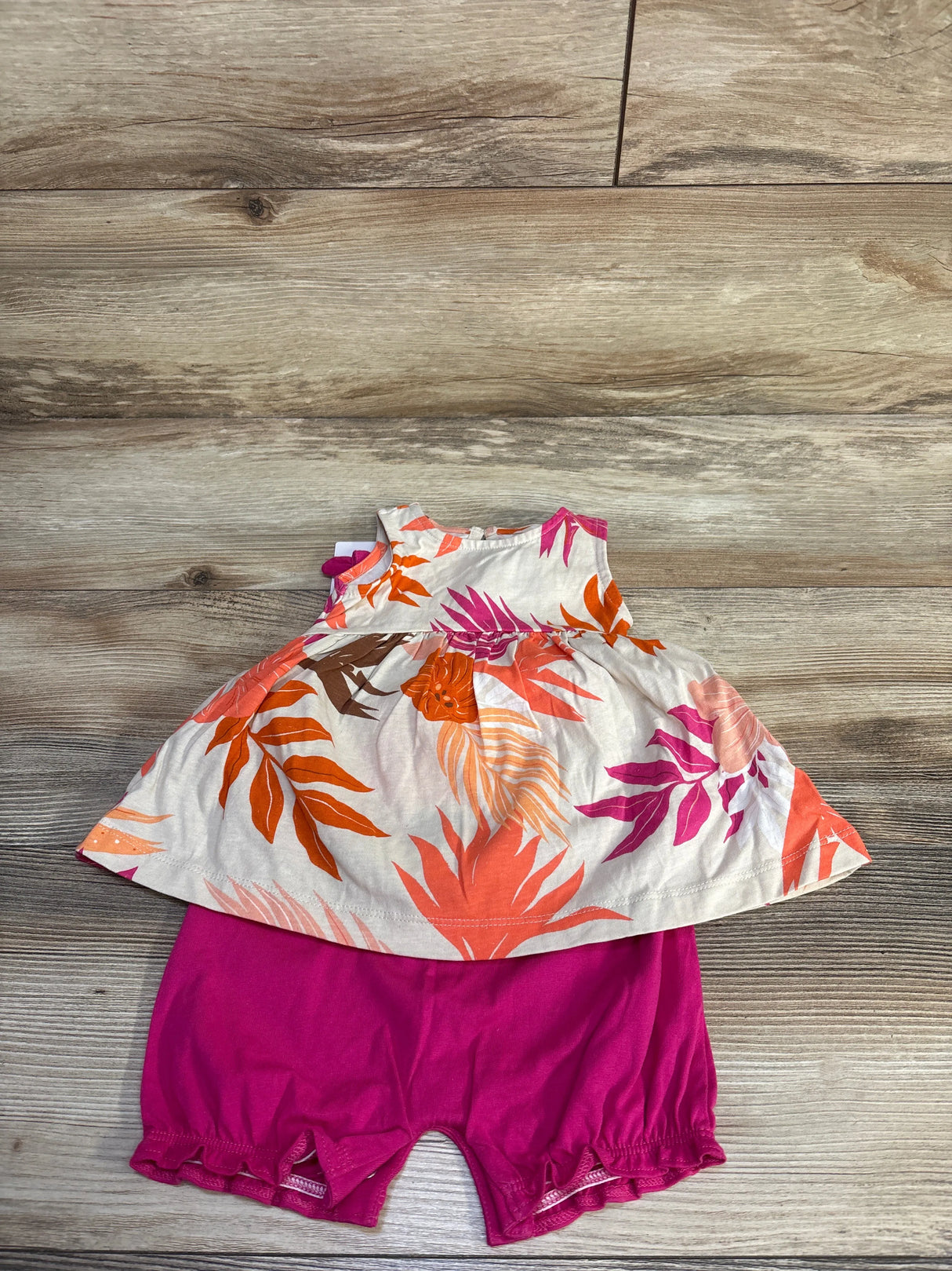 Flat lay of Carter's 3-piece dress set showcasing sleeveless beige floral top and fuchsia ruffle shorts on wood background