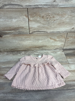 Light pink long-sleeve baby dress with textured dot pattern and ruffle detail on wooden floor