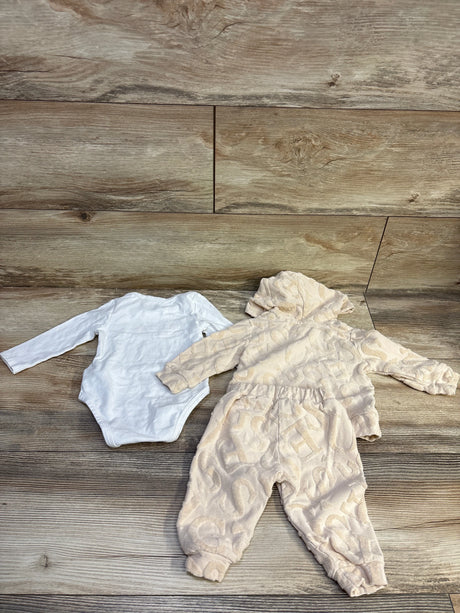 Top-down view of Guess Baby beige three-piece set with hooded patterned zip-up jacket, joggers, and white bodysuit on a wood floor