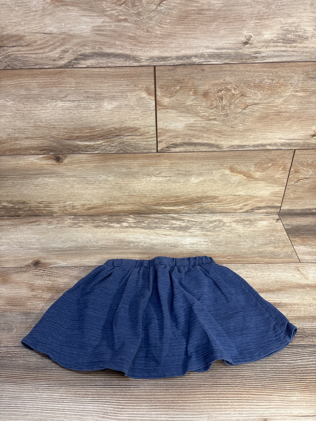 Flat lay of blue girls' drawstring skort size 4T showing elastic drawstring waist and gathered skirt on wood background