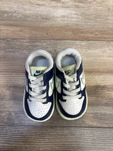 Top view of toddler Nike Dunk Low sneakers in white, midnight navy, volt tint showing laces, perforated toe on wood floor