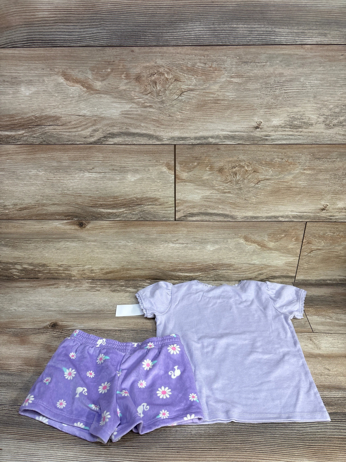 Flat-lay lilac toddler 2-piece set: short-sleeve shirt with lace trim and elastic shorts with daisy/unicorn print on wood