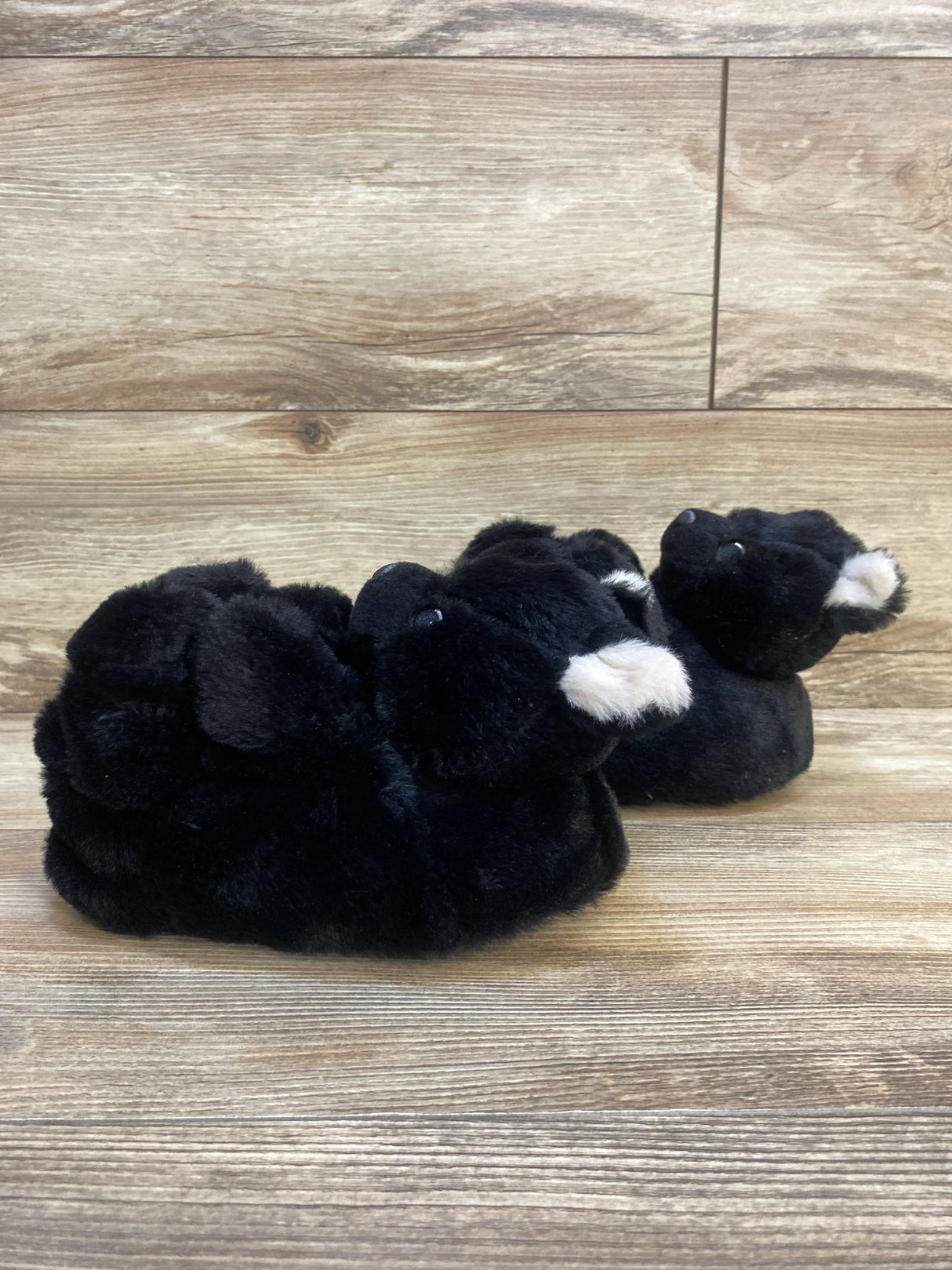 Plush black bear toddler slippers on wood floor, kids cozy footwear.