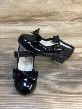 Black patent leather girls' dress shoes with bows and buckle straps on wooden floor