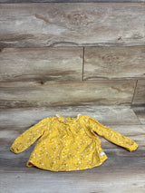 Yellow long sleeve baby top with white floral print on wood background