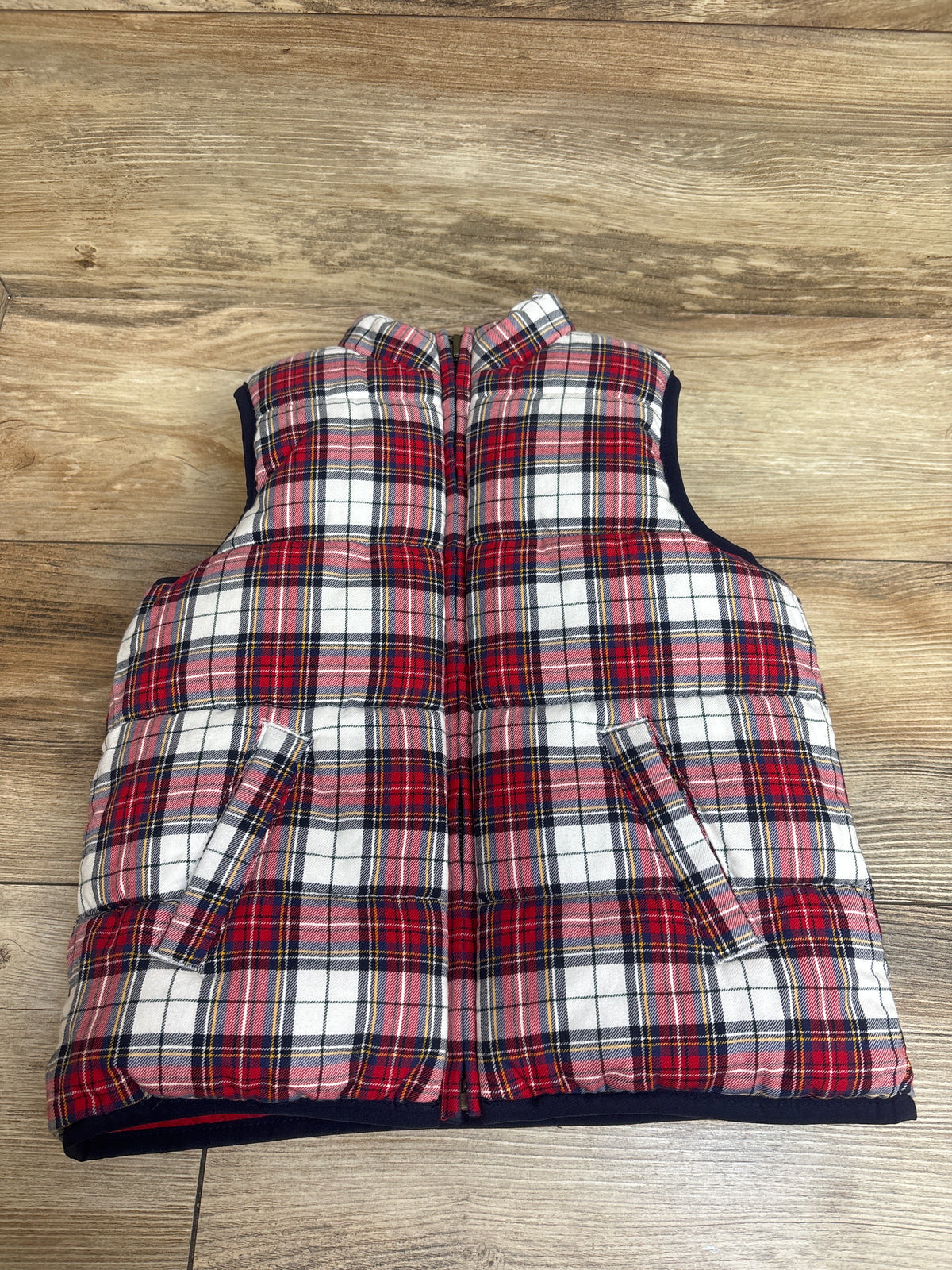 Front view of Janie and Jack reversible tartan puffer vest in red plaid with zip front and pockets on a wood background