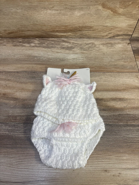 Top-down view of white crocheted unicorn baby hat and matching diaper cover showcasing ear details, pink yarn mane and small gold horn on light wood background