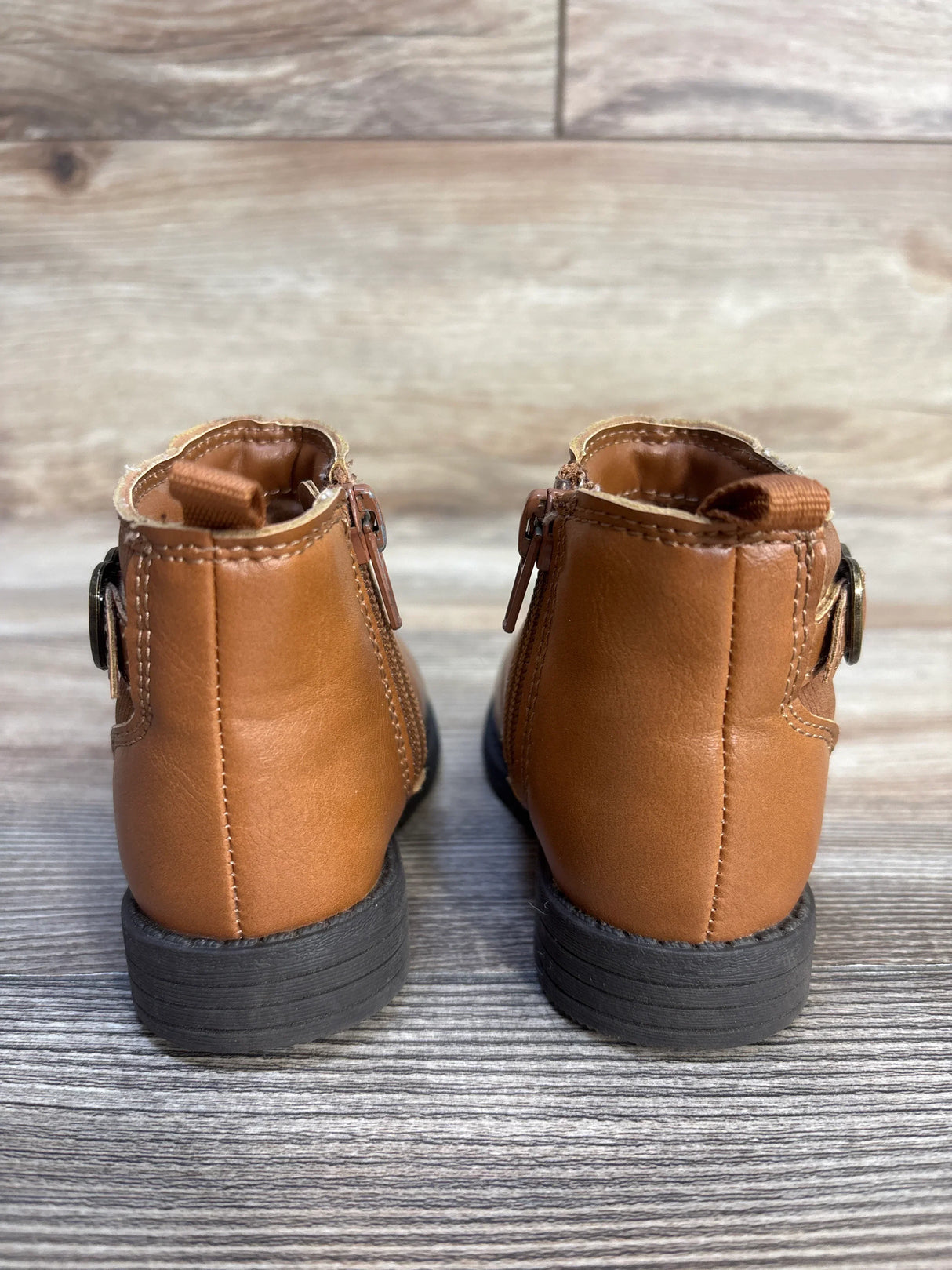 Back view of brown toddler ankle boots with zippers, rubber soles on wood floor