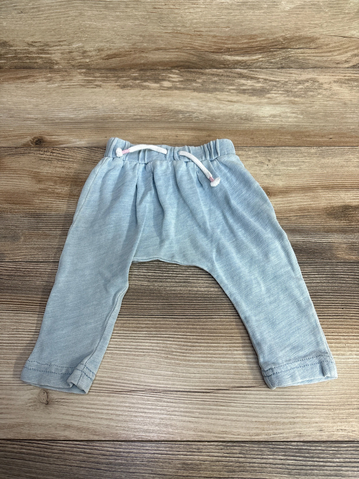 Light blue baby pants with drawstring waist on wooden background, kids clothing resale