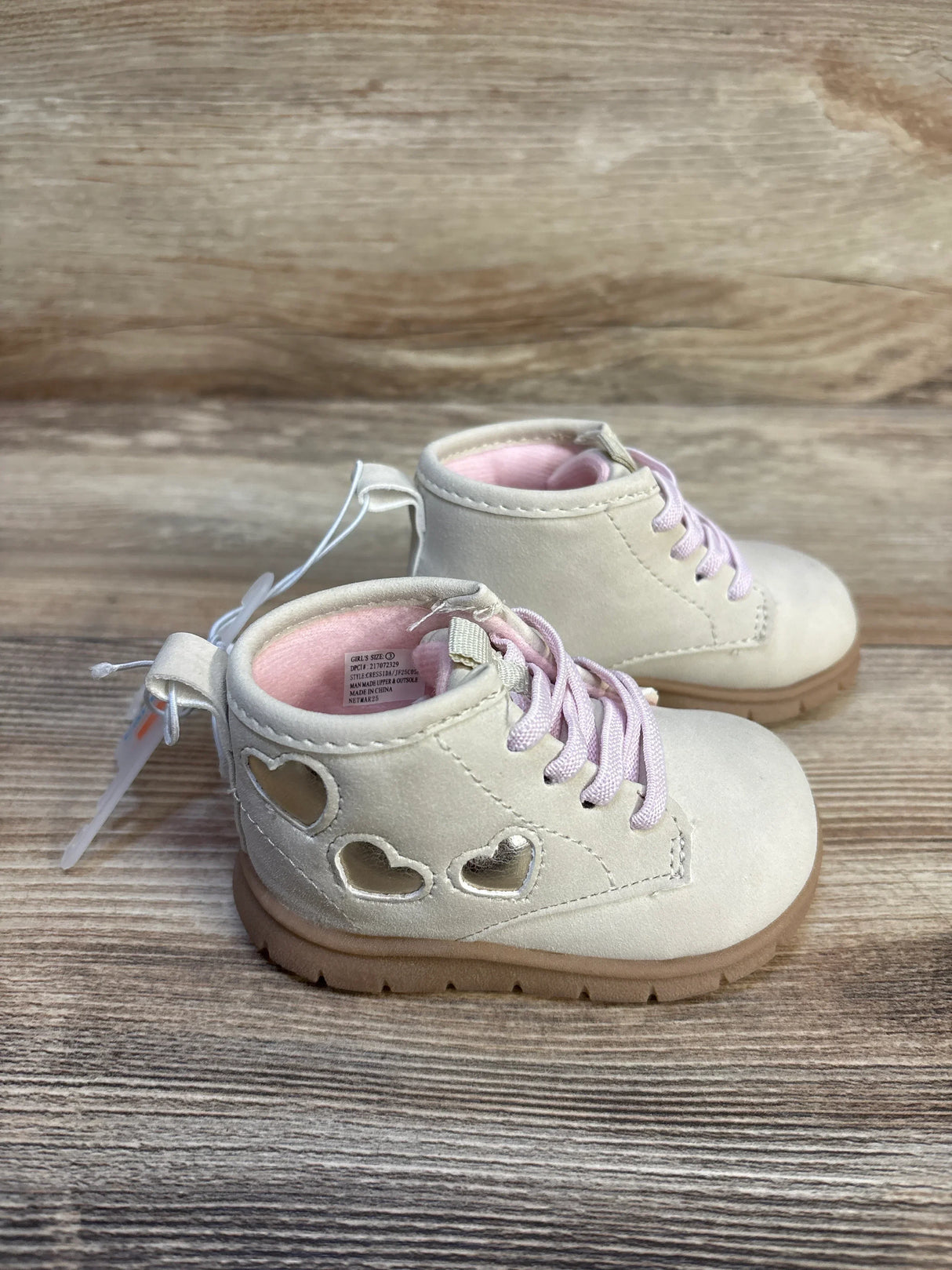 Ivory toddler boots with pink laces and heart cutouts, kids shoes on wood background