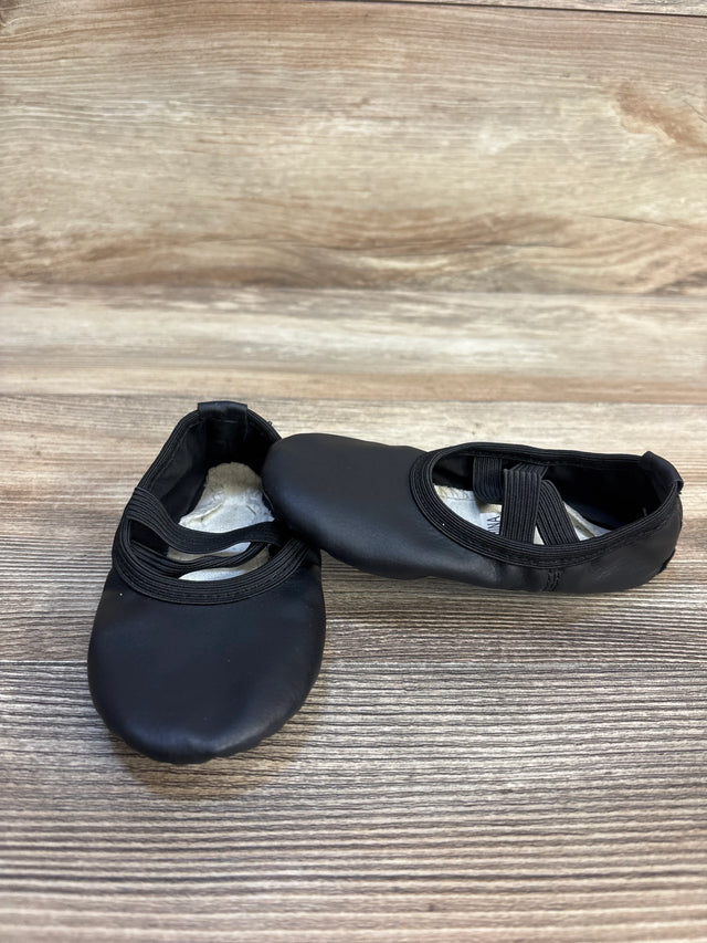 Black toddler ballet shoes with elastic straps on a wooden surface