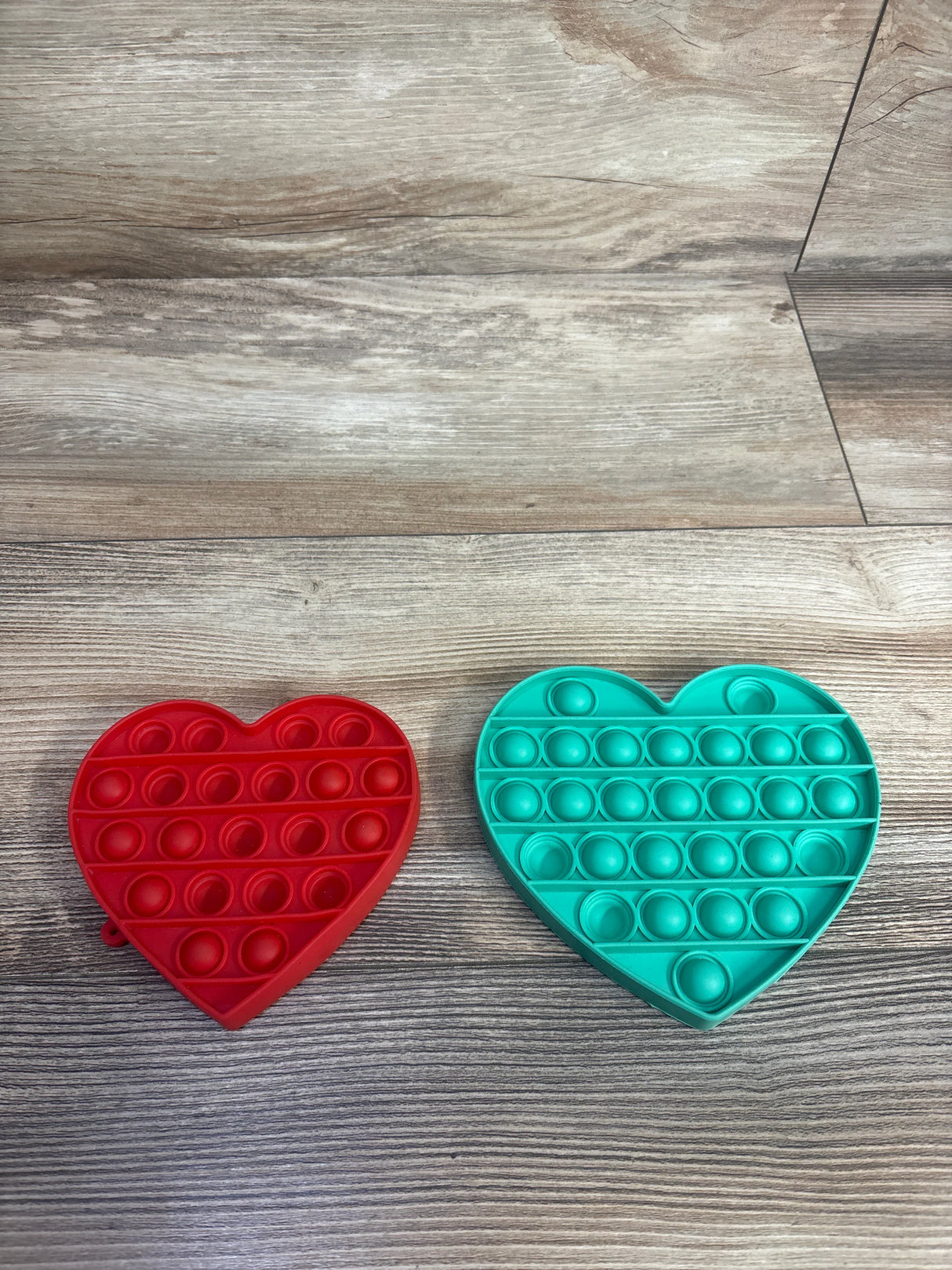 Red and teal heart-shaped pop-it fidget toys on a wood-textured surface, kids sensory toy