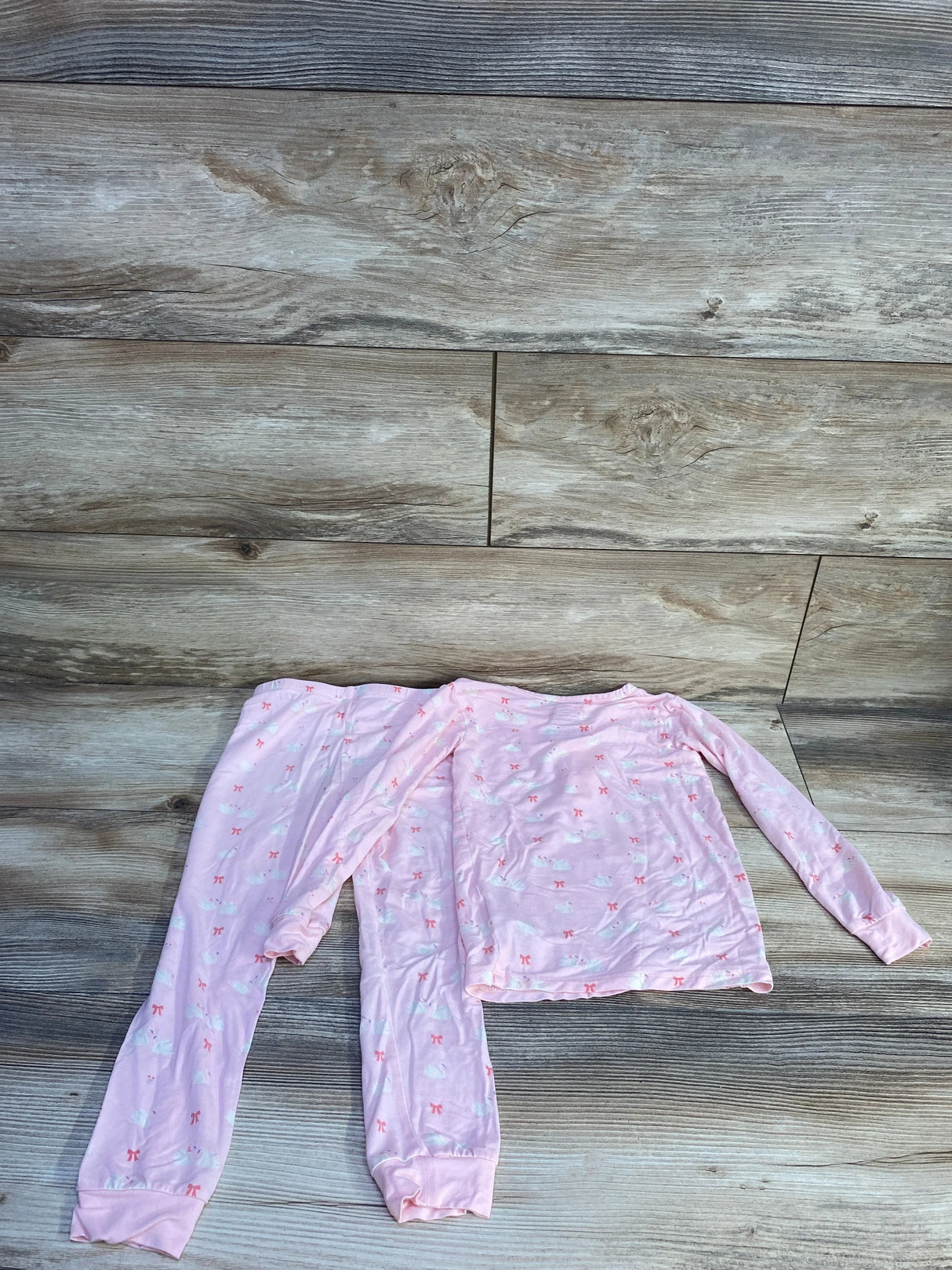 Flat lay of pink Magnetic Me 2-piece toddler pajama set (4T) showcasing long-sleeve top and elastic-cuff pants with swan and bow print on wood floor background
