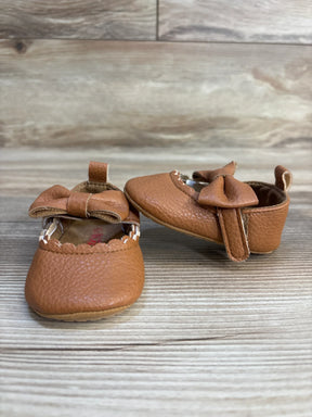 Brown leather baby shoes with bows on wooden background