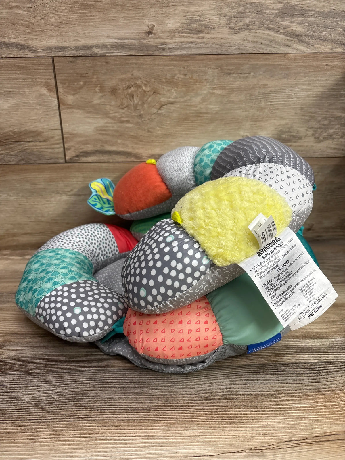 Angled view of Infantino 2-in-1 Tummy Time & Seated Support showcasing multicolored patterned cushions on a wood floor